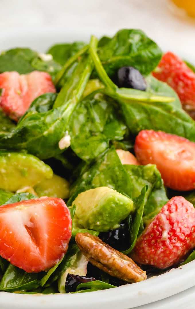 close up shot of strawberry spinach salad garnished with feta cheese on a plate