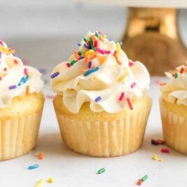 close up shot of frosted vanilla cupcakes topped with sprinkles
