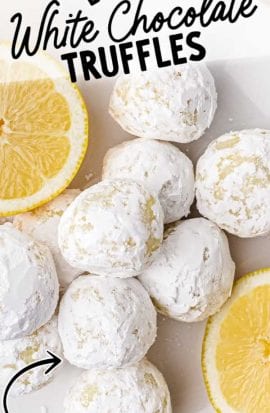 close up overhead shot of white chocolate lemon truffles dipped into powdered sugar with a bite taken out of one on a plate with lemon slices