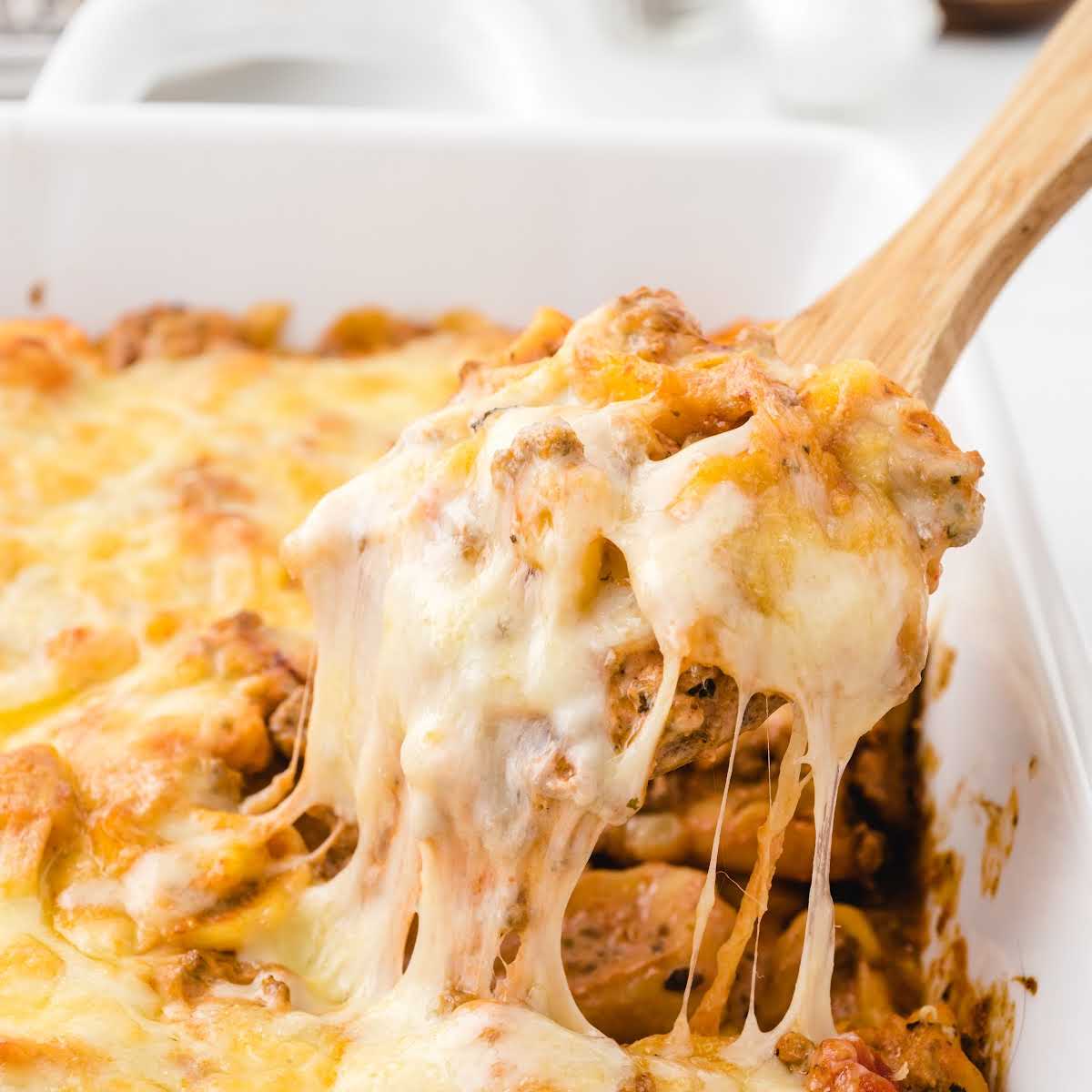 close up shot of baked tortellini topped with melted cheese in a baking dish being picked up with a wooden spoon