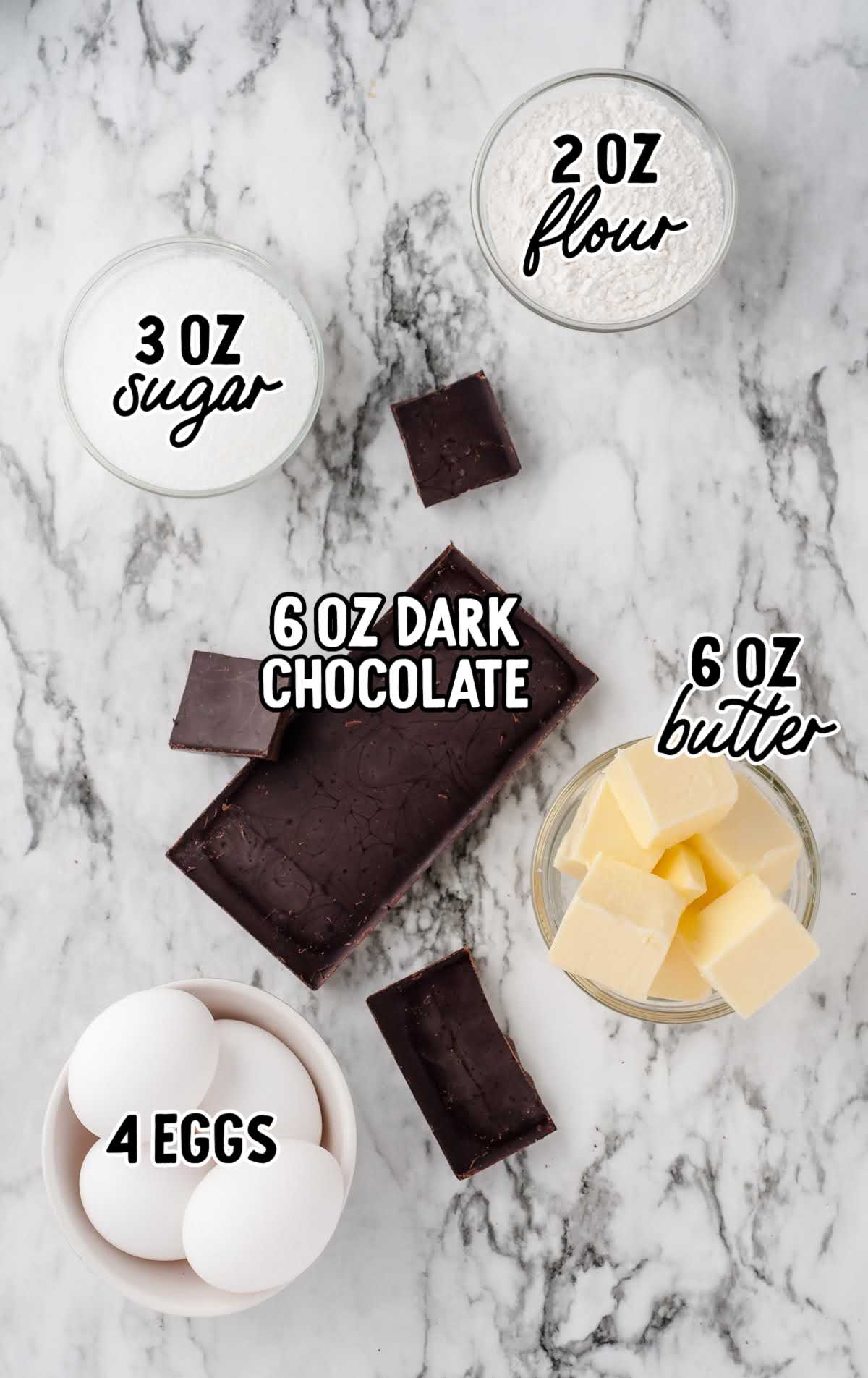 Flat lay of ingredients for lava cake including dark chocolate, butter, eggs, sugar, and flour on marble surface.