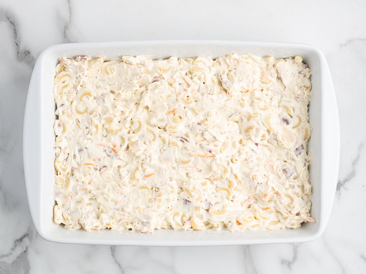 White casserole dish filled with an unbaked creamy noodle mixture, likely a Crack Chicken Casserole, on a white marble surface.
