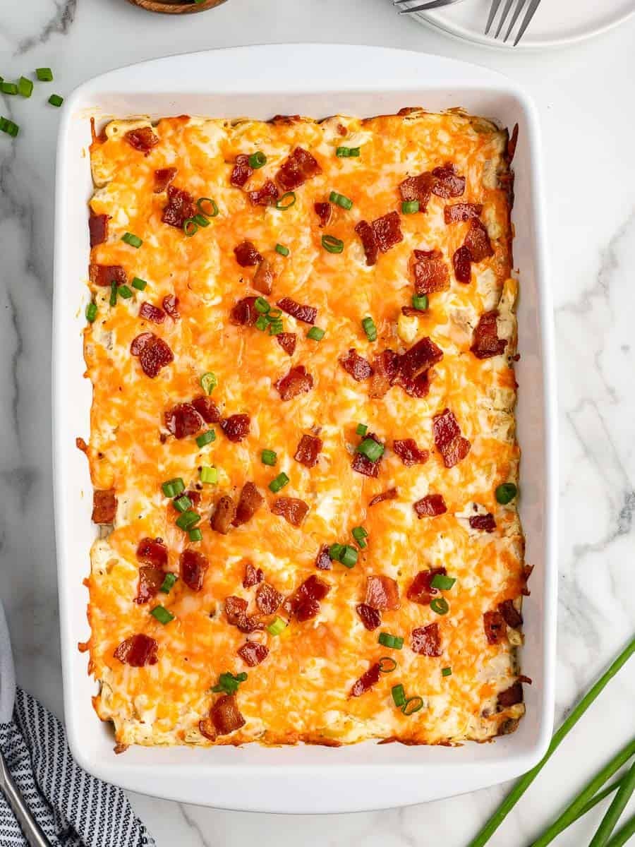 A casserole dish filled with a baked cheesy Crack Chicken Casserole, topped with melted cheese, crispy bacon pieces, and chopped green onions.