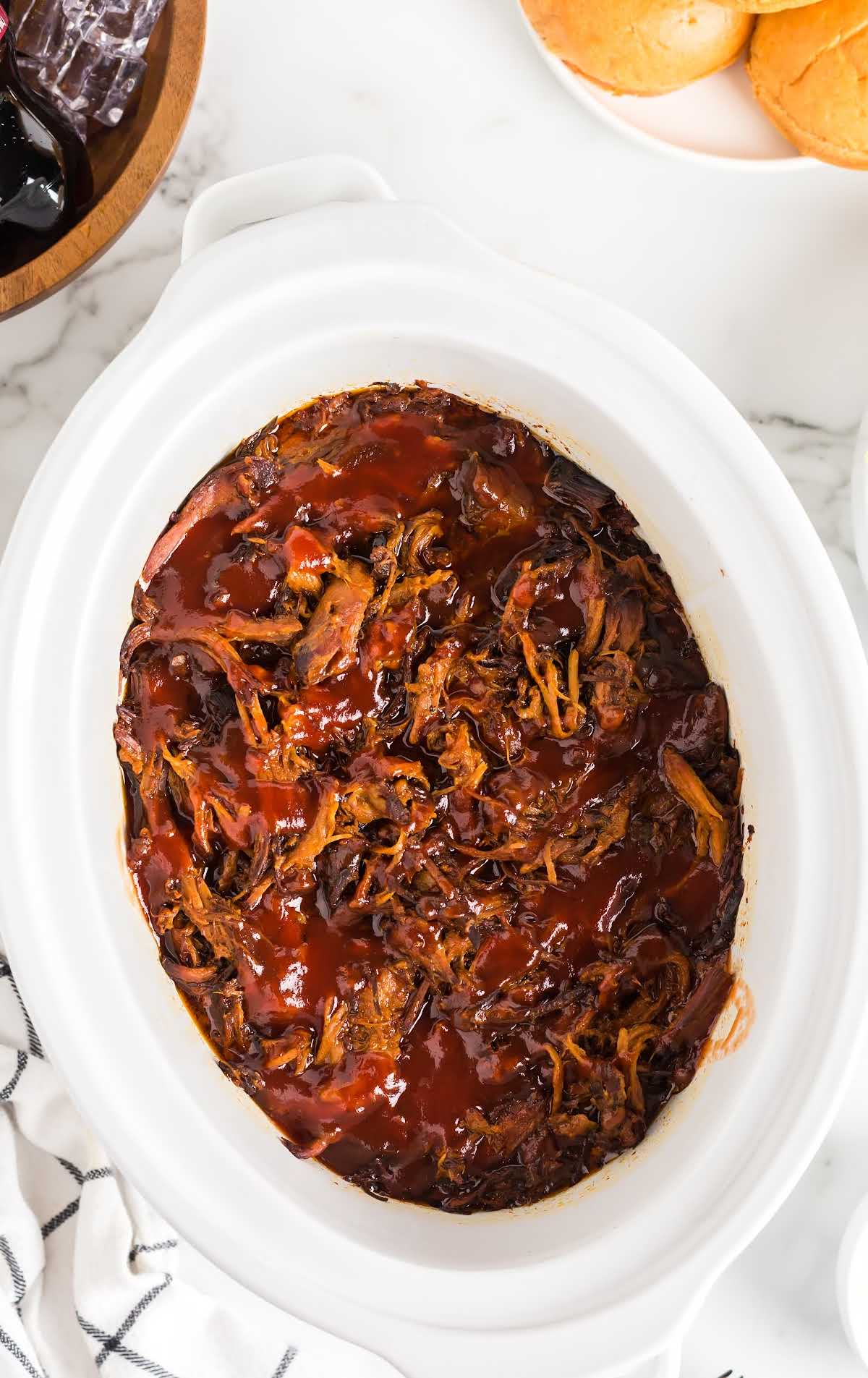 Shredded pulled pork with barbecue sauce in a white slow cooker.