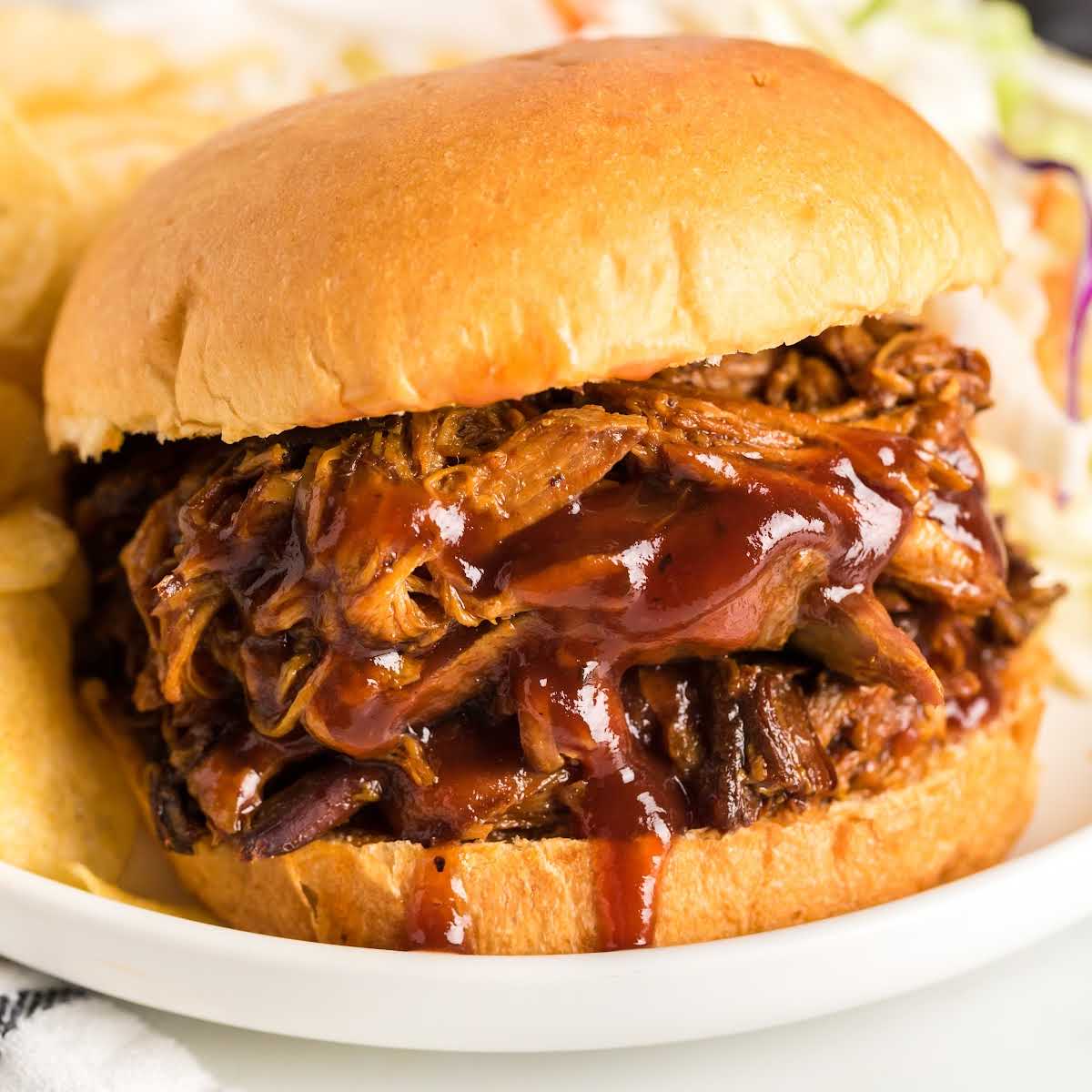 Pulled pork sandwich on a bun with BBQ sauce served with chips and coleslaw on the side.