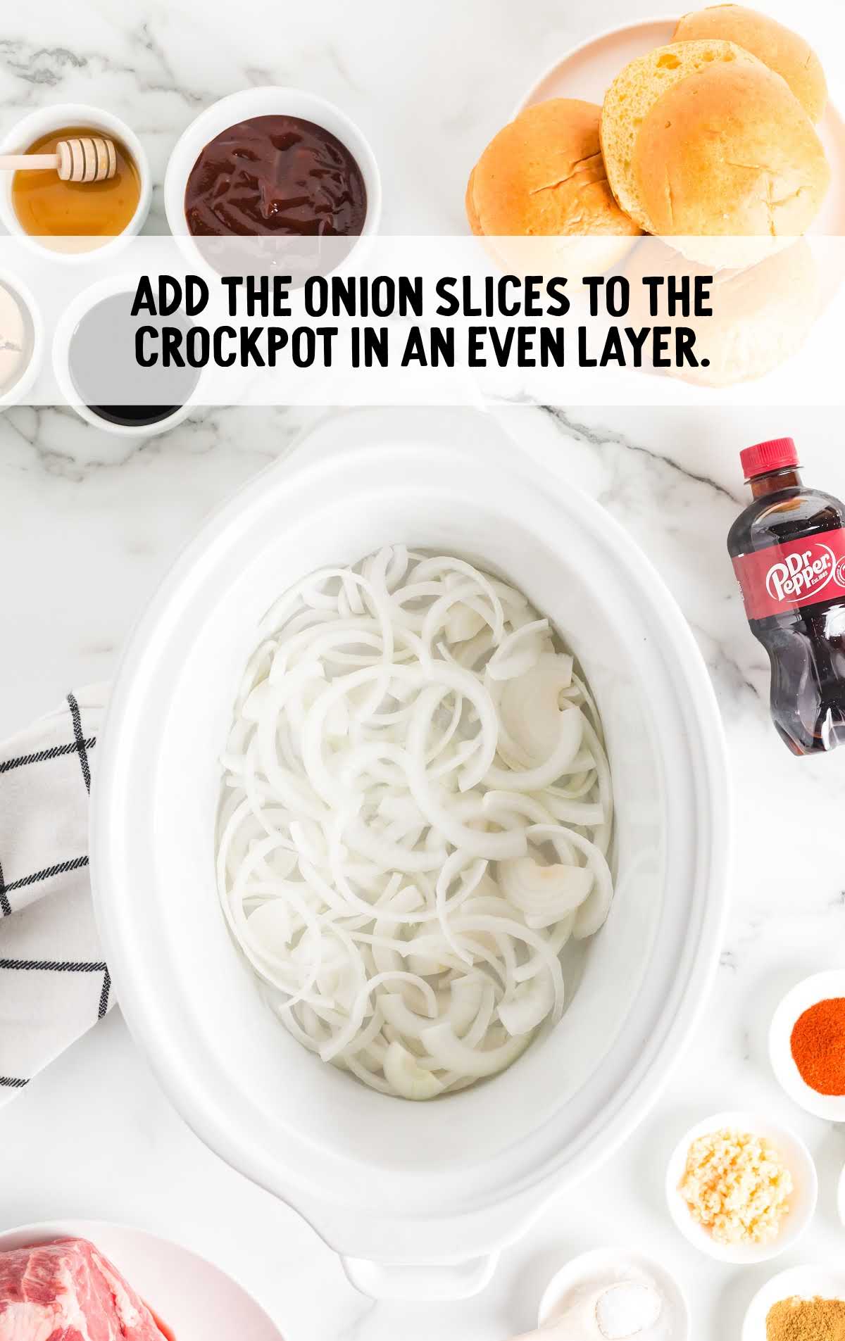 Onion slices layered in a slow cooker for pulled pork recipe.