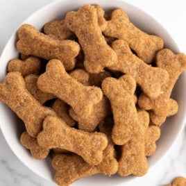 Bowl filled with homemade bone-shaped dog treats next to a small bowl of creamy peanut butter.