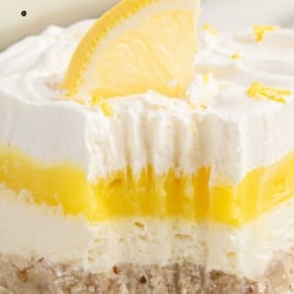 Close-up of a slice of lemon lush dessert with creamy layers, lemon pudding, and a lemon wedge garnish, labeled “50’s vintage lemon lush – you won’t believe how good this is!”