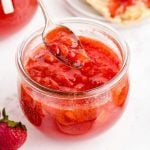 close up shot of strawberry freezer jam in a glass jar with a spoon