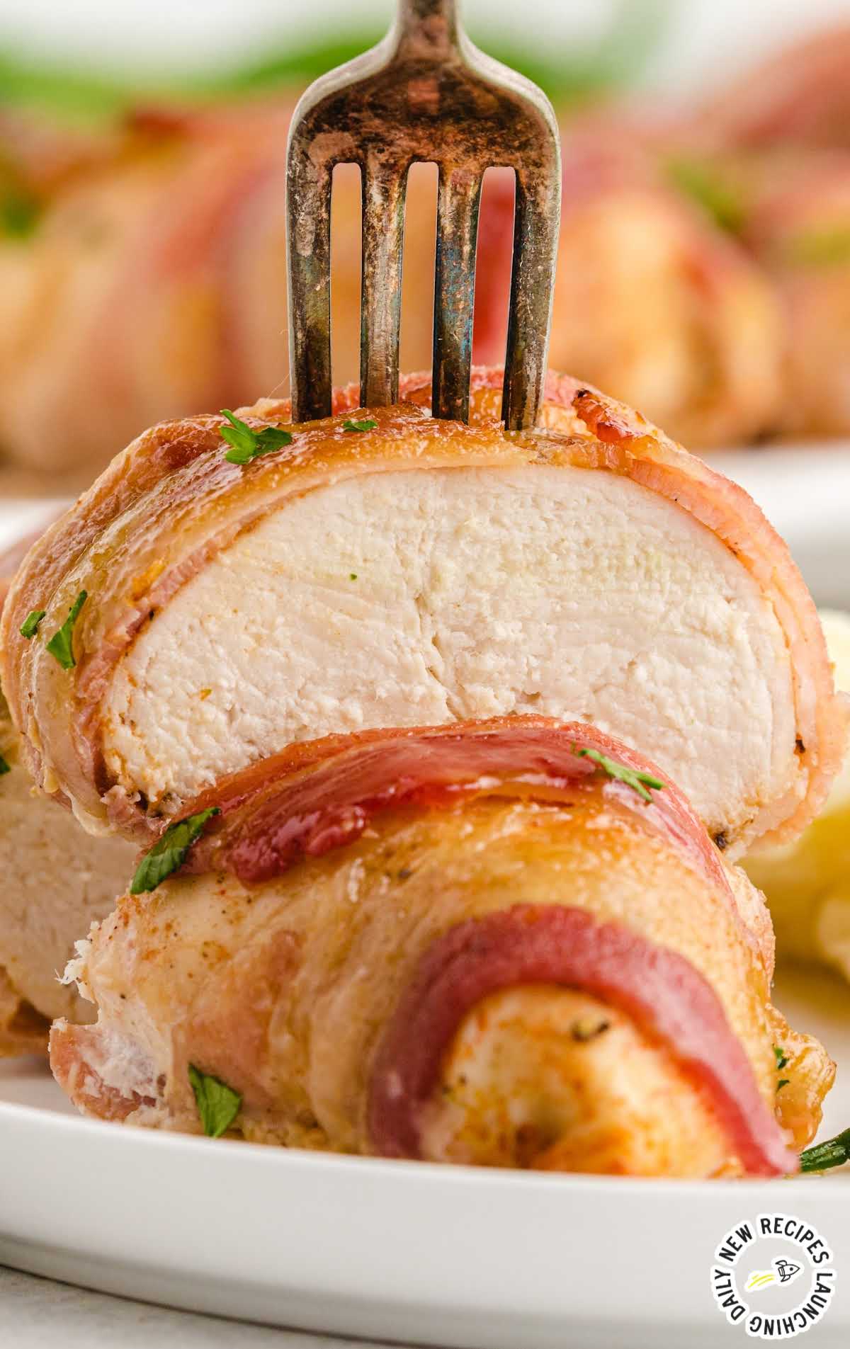 close up shot of Bacon-Wrapped Chicken garnished with parsley on a fork