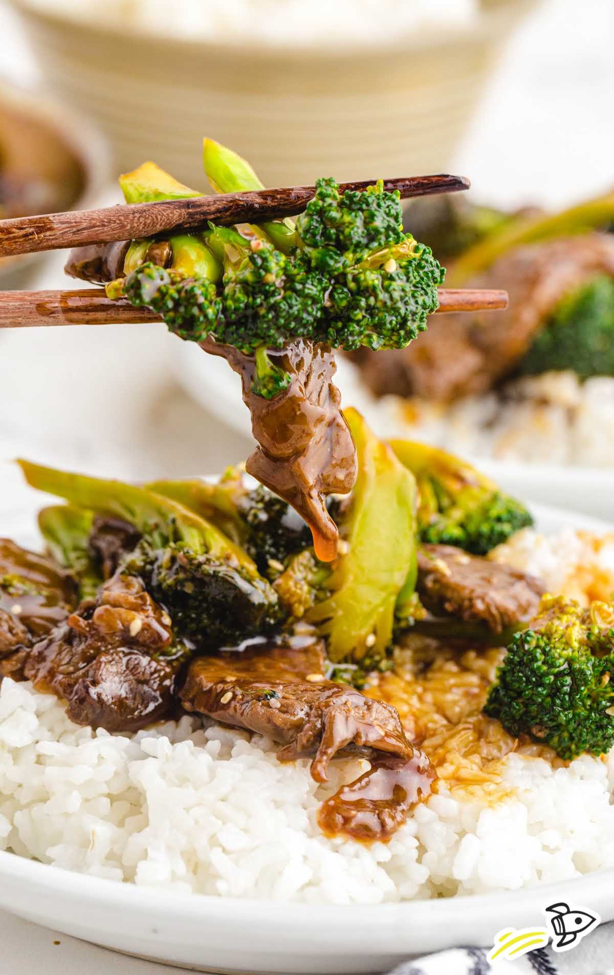 beef and broccoli on a plate of rice being picked up with chopsticks
