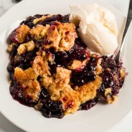 a piece of Blueberry Dump Cake served with vanilla ice cream on a plate