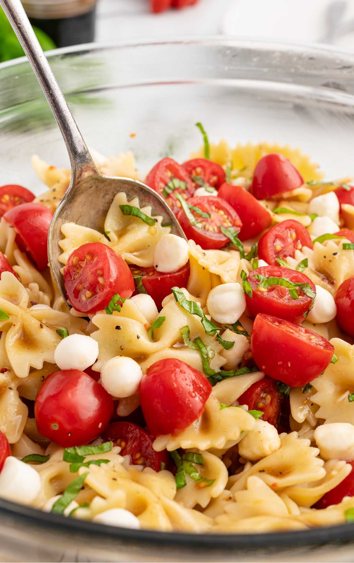 Caprese pasta salad topped with basil in a bowl with a spoon
