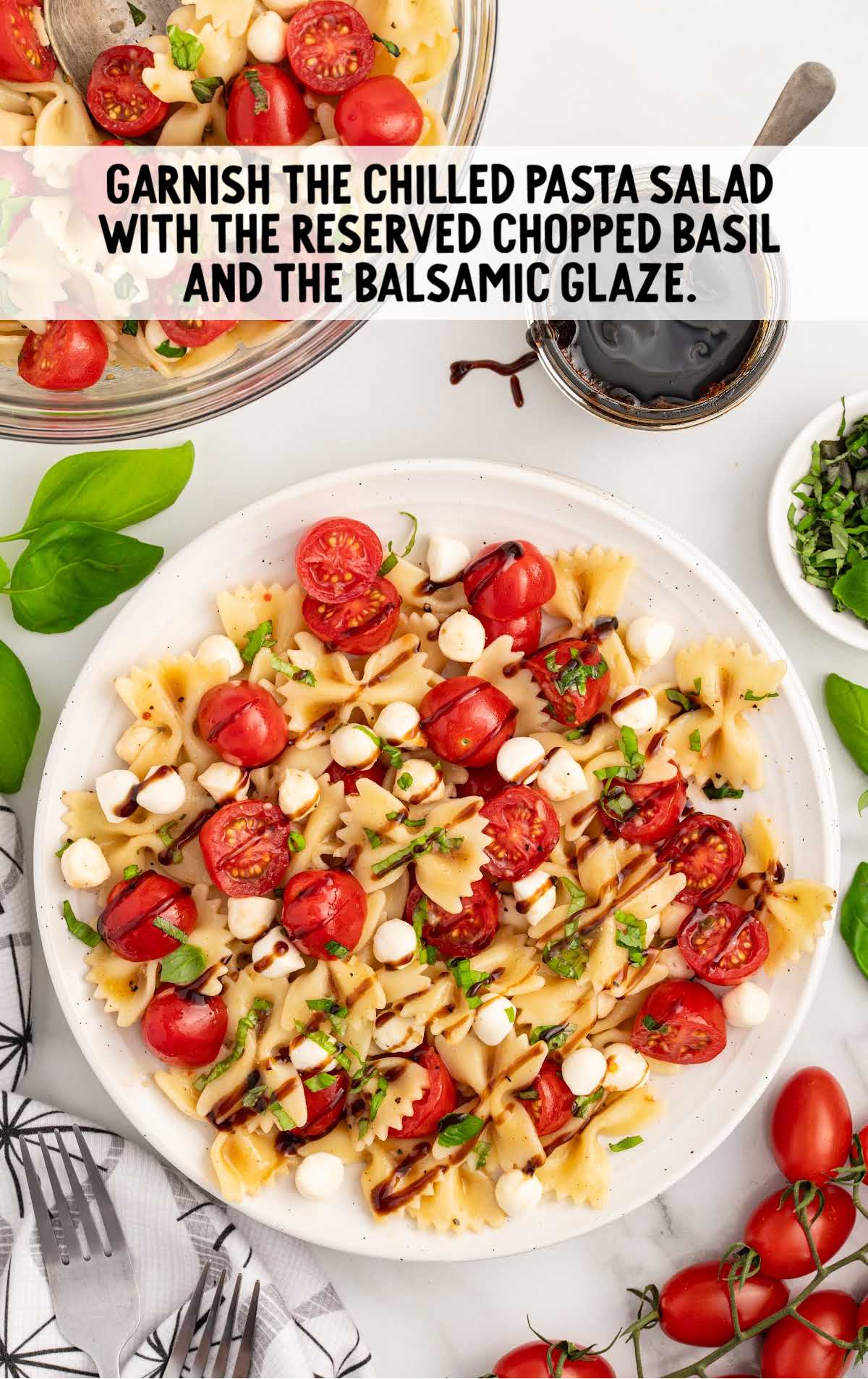 a plate of caprese pasta salad being topped with balsamic glaze and basil