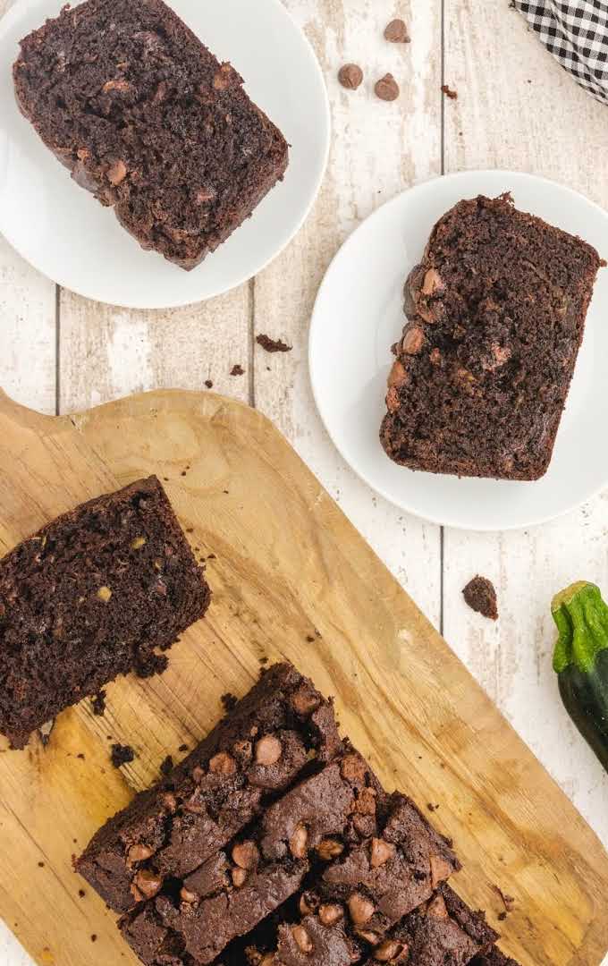 close up shot of slices of chocolate zucchini bread with chocolate chips on a wooden board and slices served on a plate