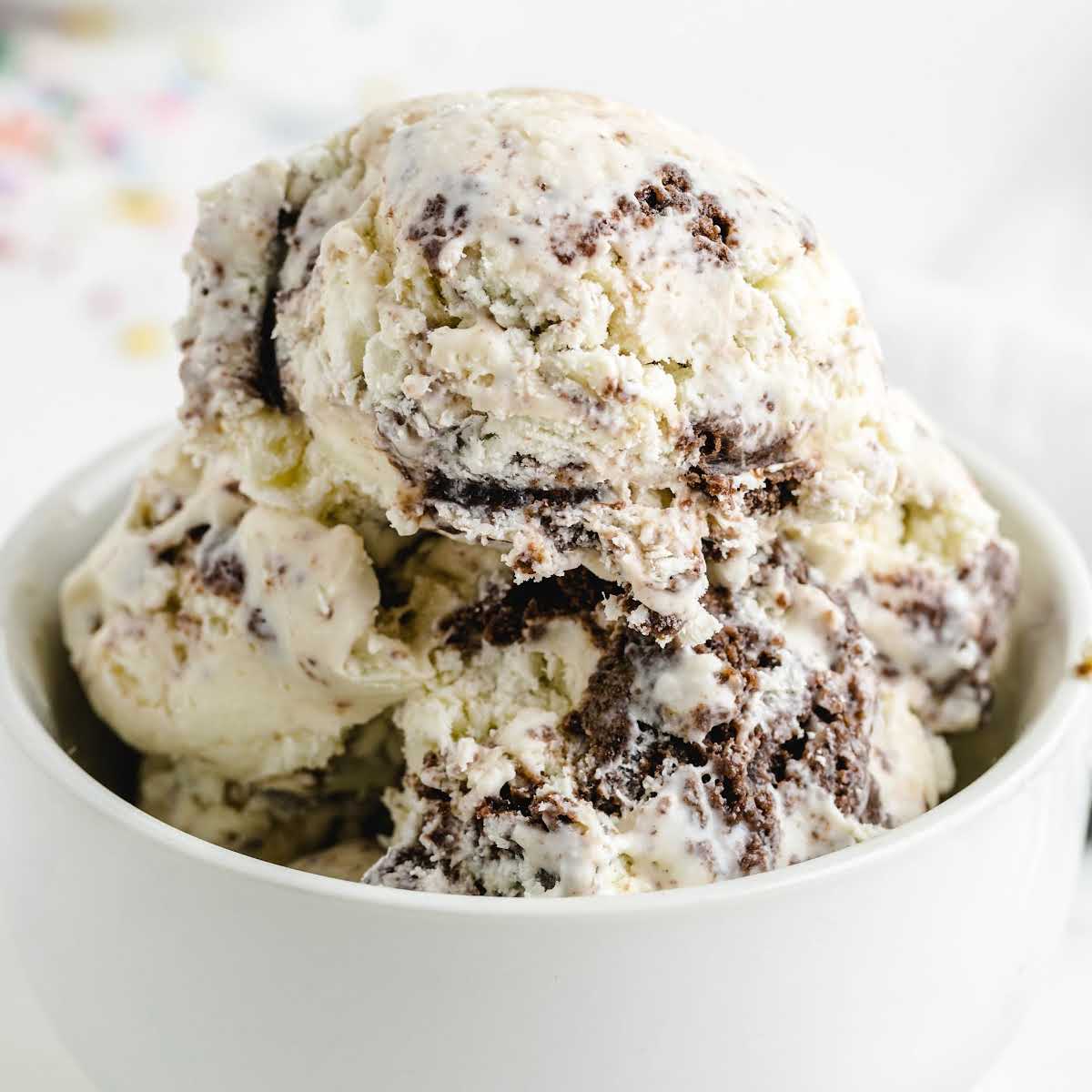 Close-up scoop of cookies and cream ice cream in a bowl with chocolate cookie chunks throughout.