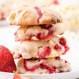 Stack of strawberry cream cheese cookies on a white plate with fresh strawberries scattered nearby.