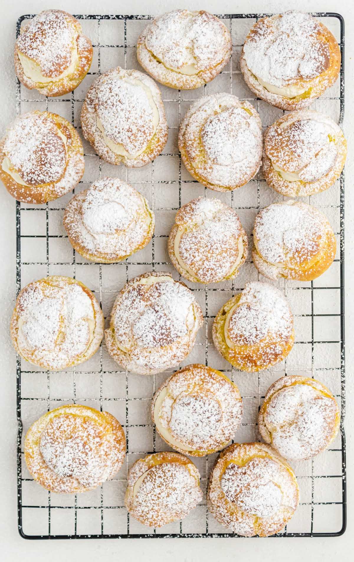 Overhead view of multiple cream puffs arranged on a wire rack, lightly dusted with powdered sugar.