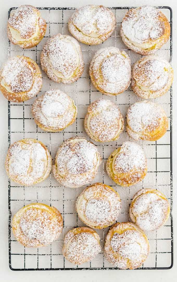 close up overhead shot of cream puffs sprinkled with powdered sugar on a closing rack