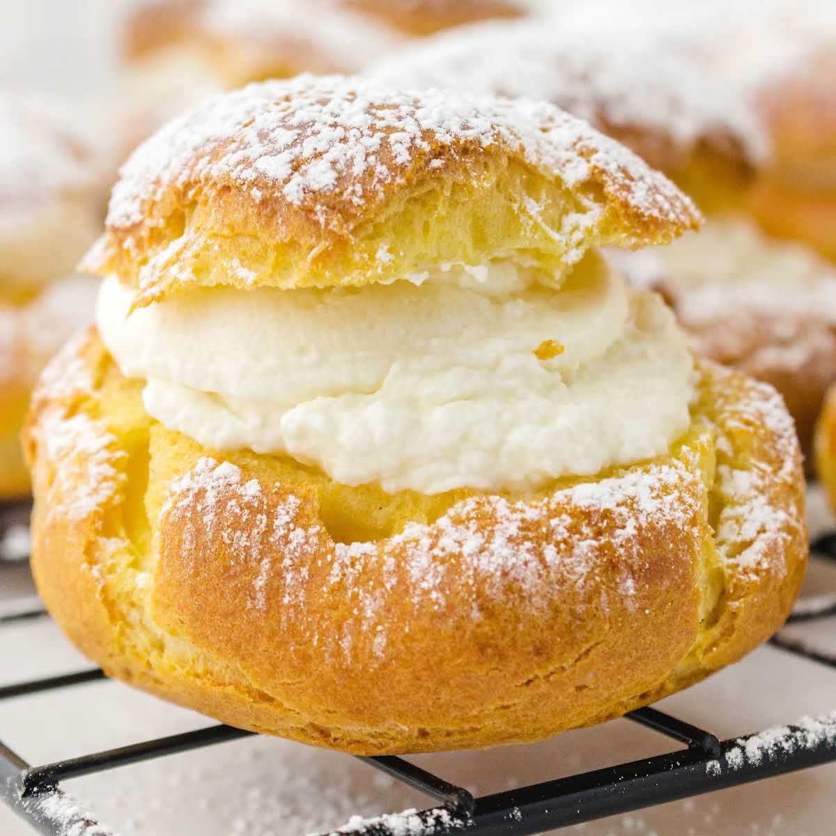 Close-up of a cream puff on a cooling rack, filled with vanilla cream and topped with powdered sugar.
