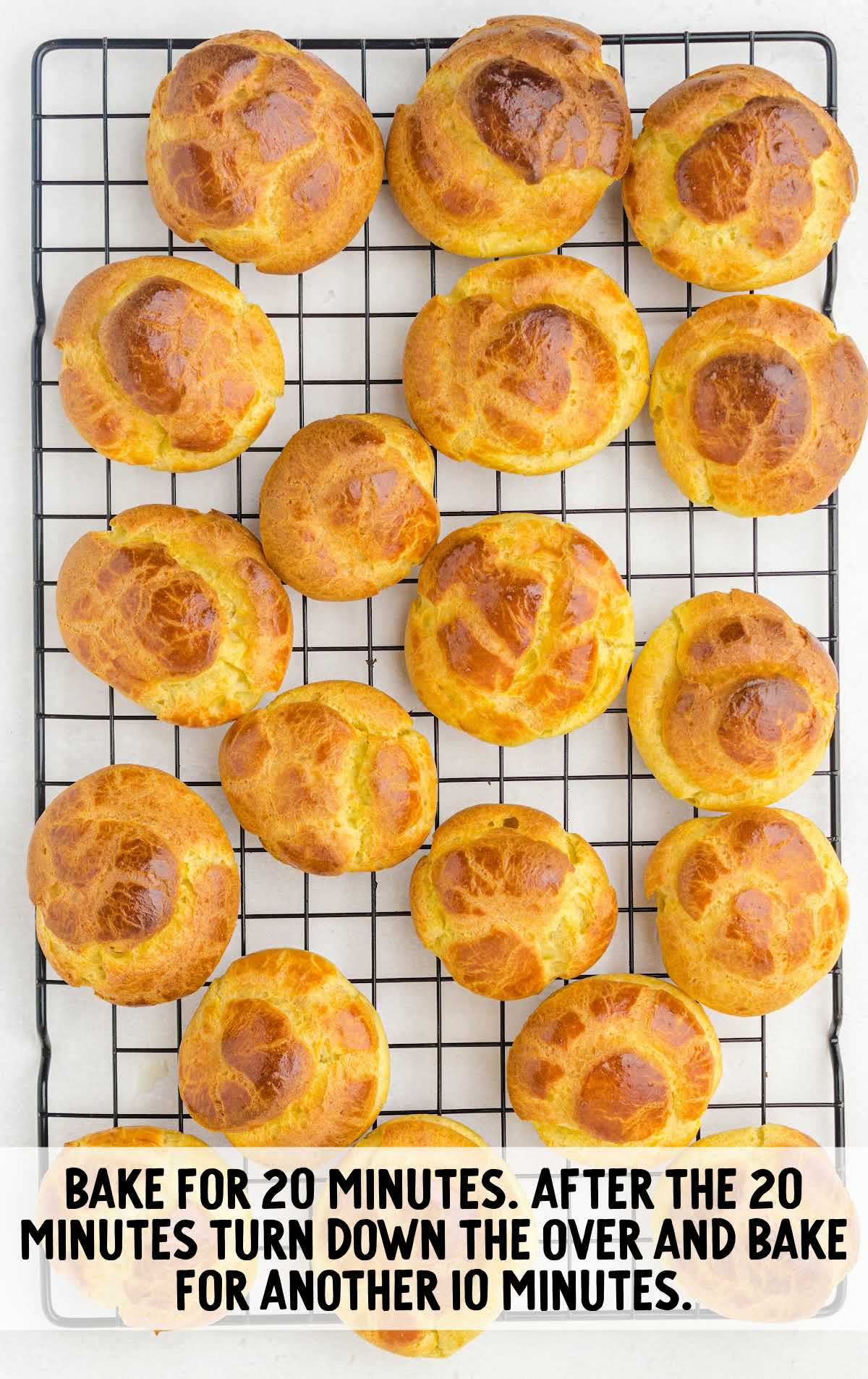 Golden brown baked cream puffs cooling on a wire rack after 30 minutes in the oven.