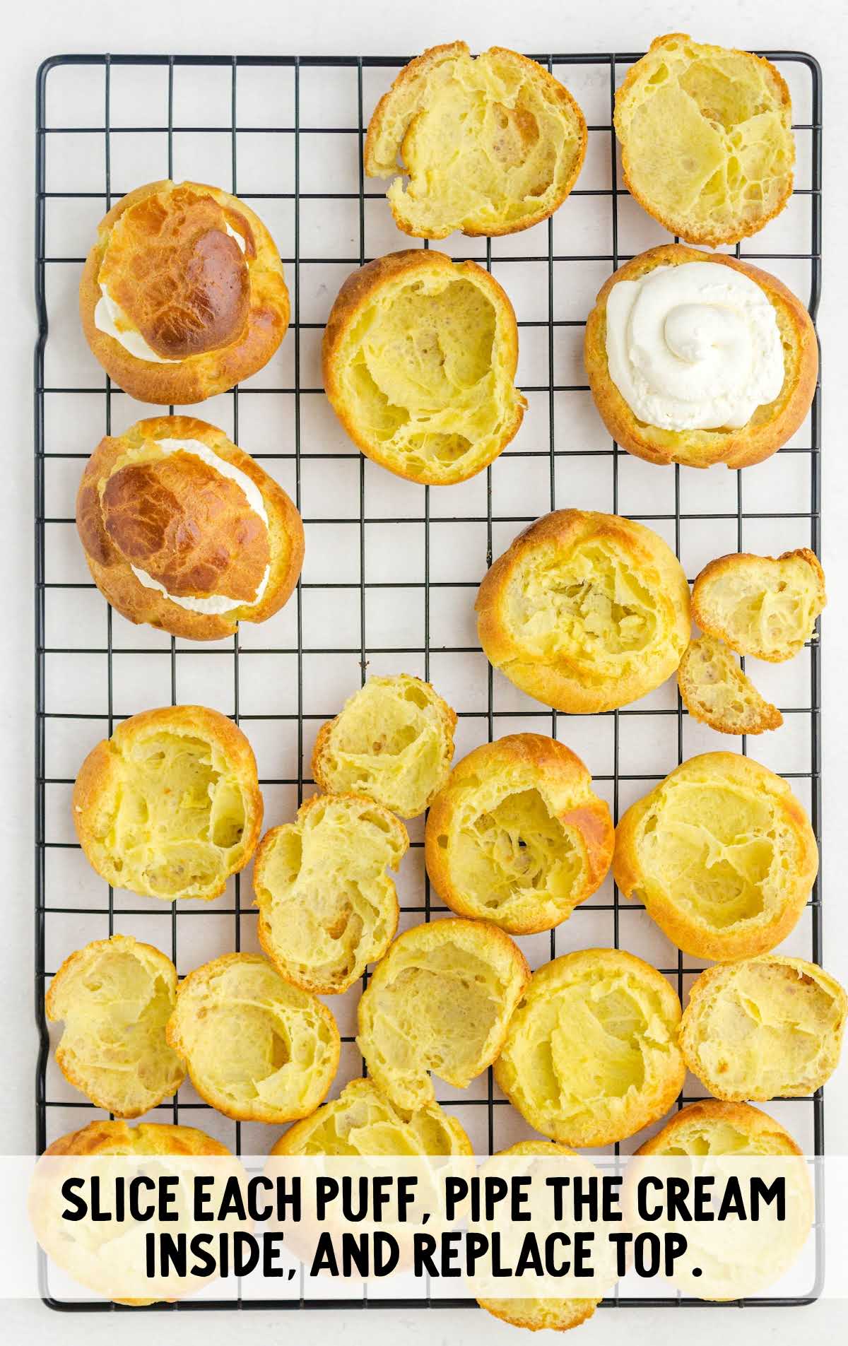 Cream puffs sliced open on a cooling rack, with cream being piped into the hollow centers before replacing the tops.