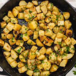 overhead shot of a skillet of fried potatoes garnished with parsley