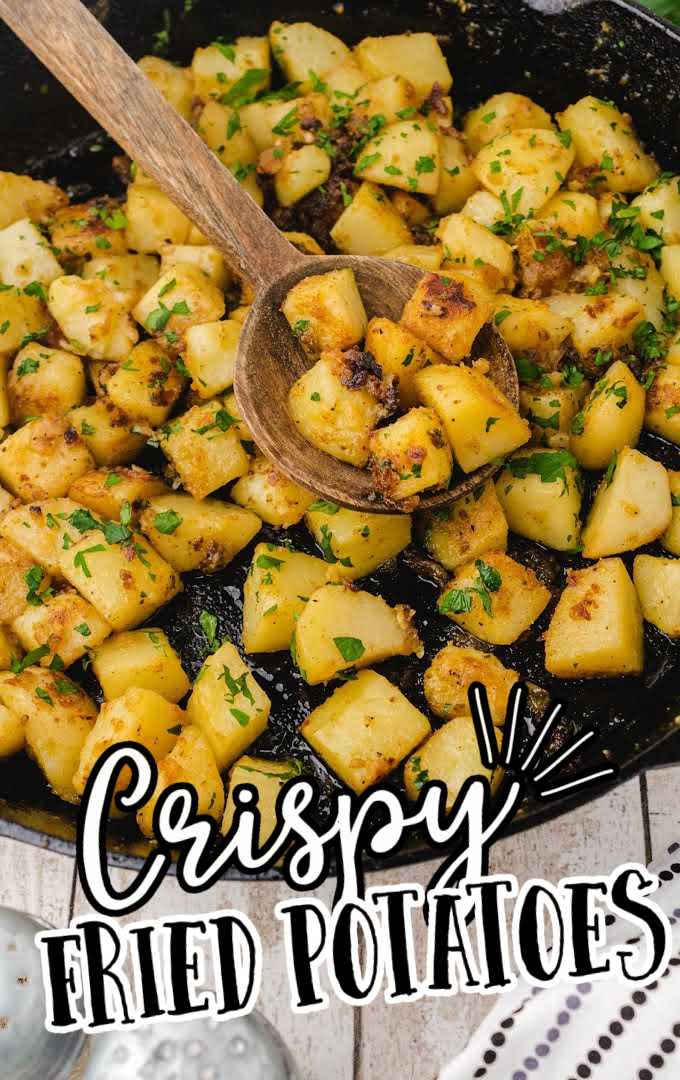 close up shot of crispy fried potatoes garnished with parsley in a skillet with a large wooden spoon