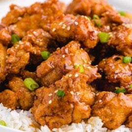 close up shot of a plate of Crispy Honey Chicken garnished with green onions and served over white rice