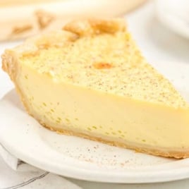 A close-up of a single slice of custard pie on a white plate, highlighting its smooth texture and golden crust.