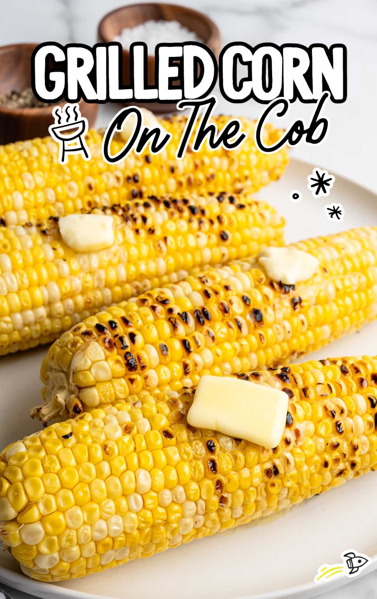 Grilled corn on the cob topped with melting butter on a white plate with text overlay “Grilled Corn on the Cob.”