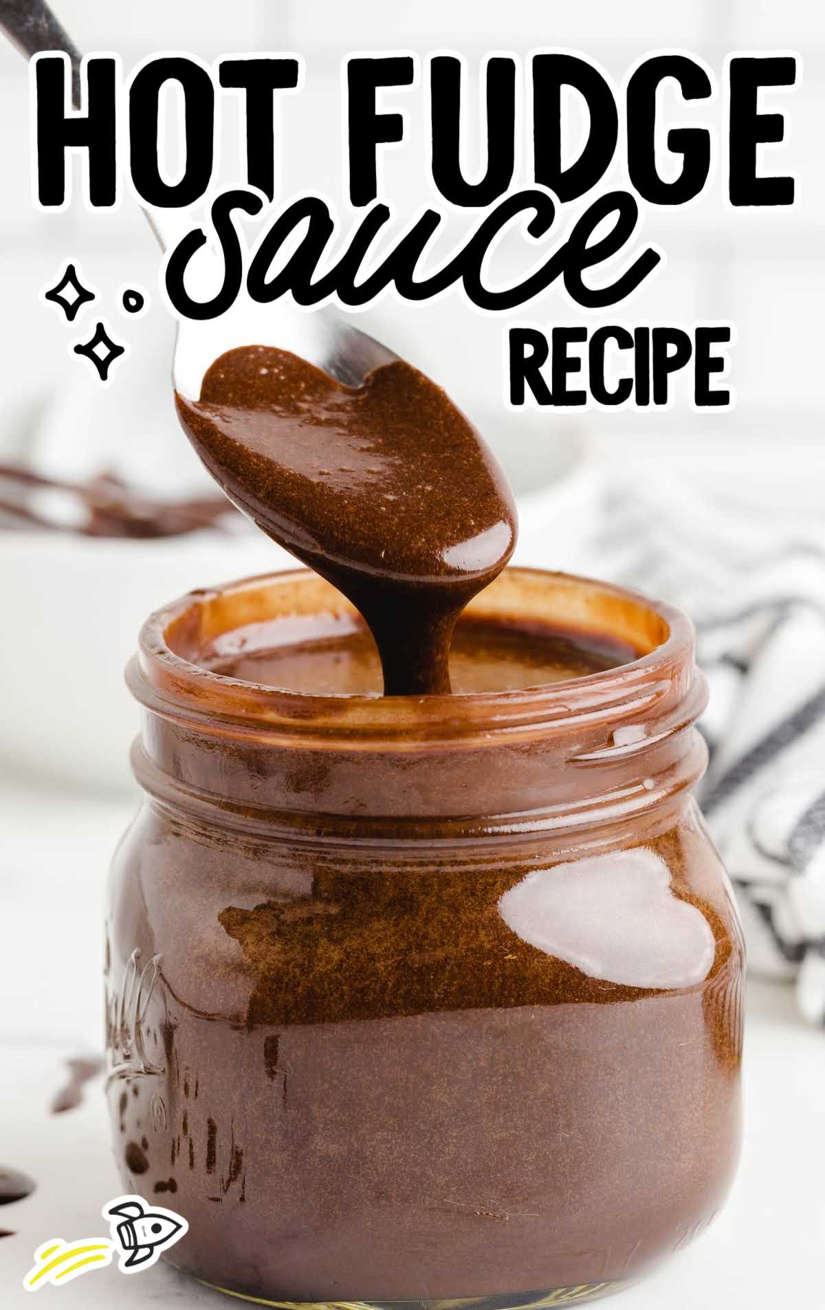 side shot of hot fudge sauce being poured with a spoon into a mason jar