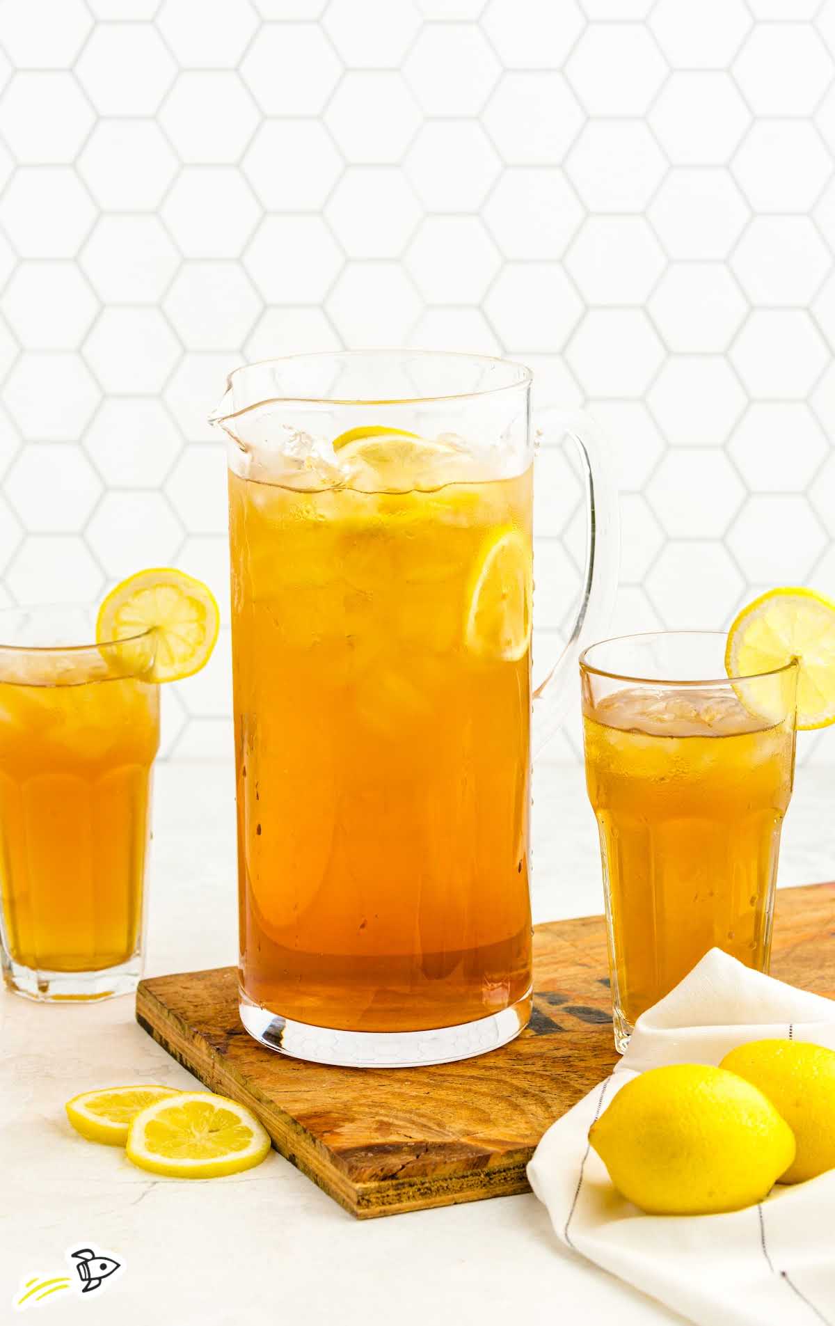 Pitcher and two glasses of iced tea with lemon slices on a wooden board and white background