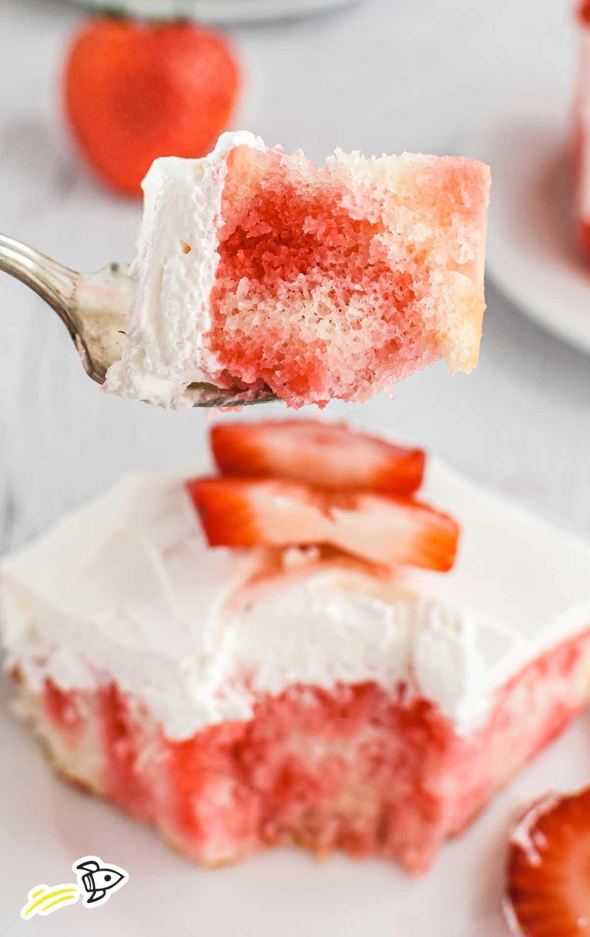 close up shot of a slice of jello poke cake topped with whipped cream and strawberry slices with a piece on a fork