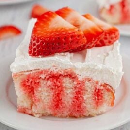 close up shot of a slice of jello poke cake topped with whipped cream and strawberry slices on a plate