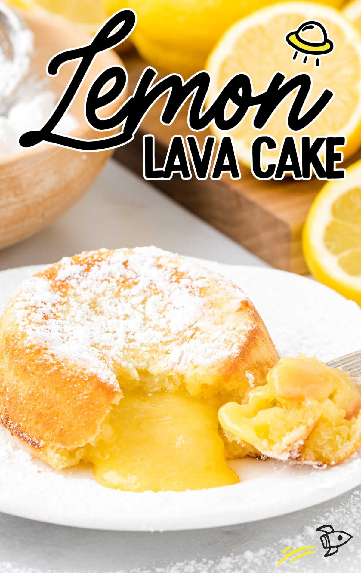 close up shot of a lemon lava cake dusted with powdered sugar with a bite taken out showing its inside lemon layers on a white plate