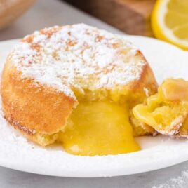 close up shot of a lemon lava cake dusted with powdered sugar with a bite taken out showing its inside lemon layers on a white plate