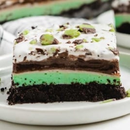 Full slice of mint chip dessert lasagna on a white plate with visible creamy layers and chocolate mint topping.