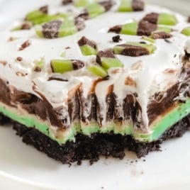 Flat lay of mint chip dessert lasagna ingredients including Oreos, cream cheese, chocolate pudding mix, whipped topping, mint chocolate chunks, and powdered sugar.