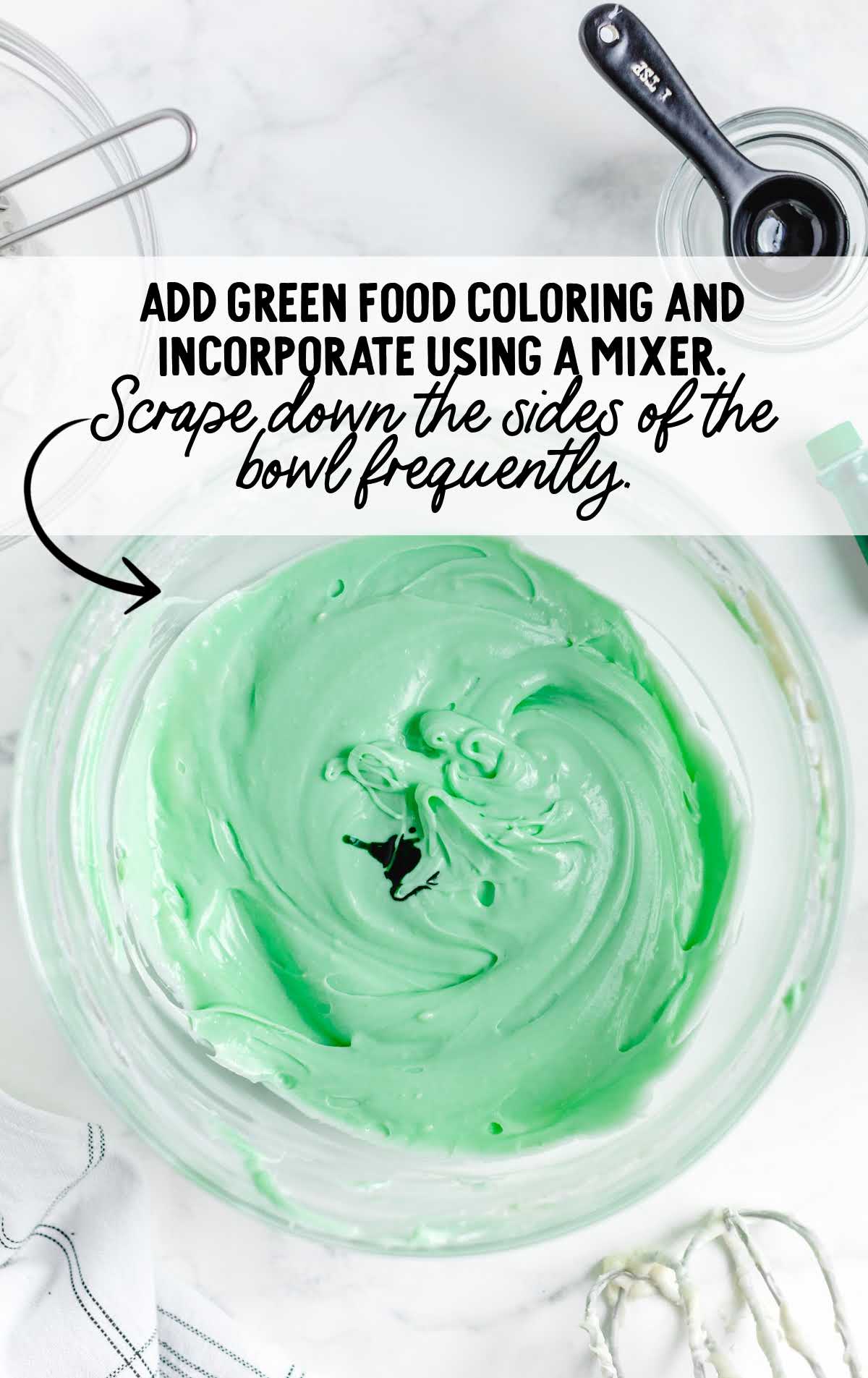 Green-tinted cheesecake mixture in a bowl with food coloring being incorporated for the mint layer.