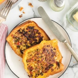Overhead image of two slices of cooked omelet in a hole toast with butter and silverware nearby.