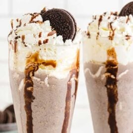 close up shot of glasses of Oreo milkshake topped with a Oreo and chocolate glaze falling down the cup