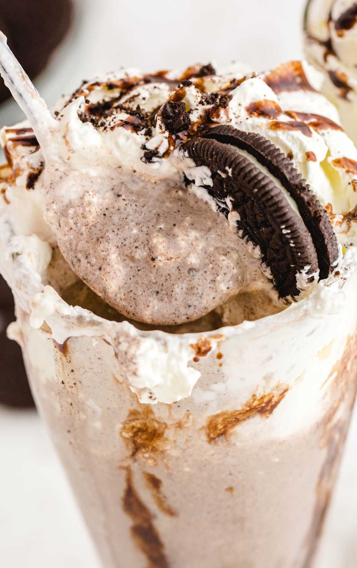 close up shot of a glass of Oreo milkshake topped with a Oreo and chocolate glaze falling down the cup