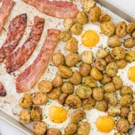 Overhead shot of a sheet pan filled with crispy bacon, roasted baby potatoes, and baked eggs garnished with parsley