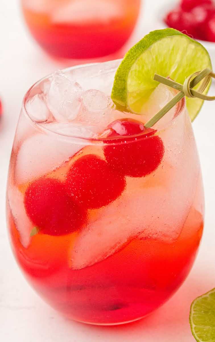 close up shot of a glass of Shirley Temple garnished with cherries and a lime slice