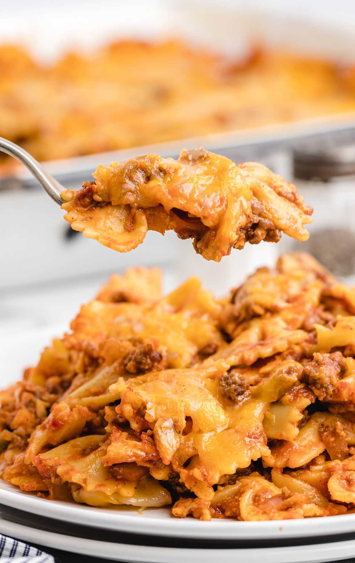 Fork lifting a bite of sloppy joe casserole from a white plate, showing pasta, ground beef, and melted cheese.