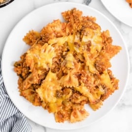 Overhead shot of a serving of baked sloppy joe casserole on a white plate, with melted cheese and bowtie pasta.