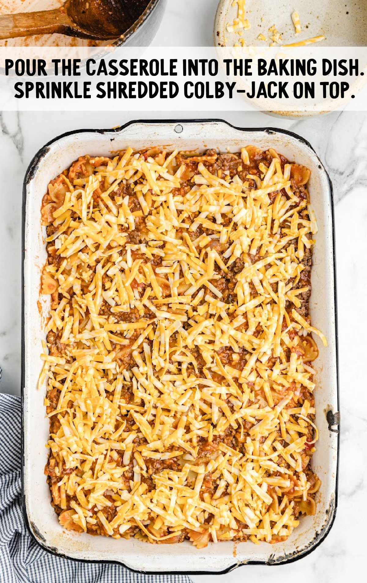 Unbaked sloppy joe casserole in a dish, topped with shredded Colby-Jack cheese, ready to go into the oven.
