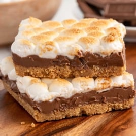 Two s’mores bars stacked on a wooden board with gooey chocolate and toasted marshmallows on a graham cracker crust.