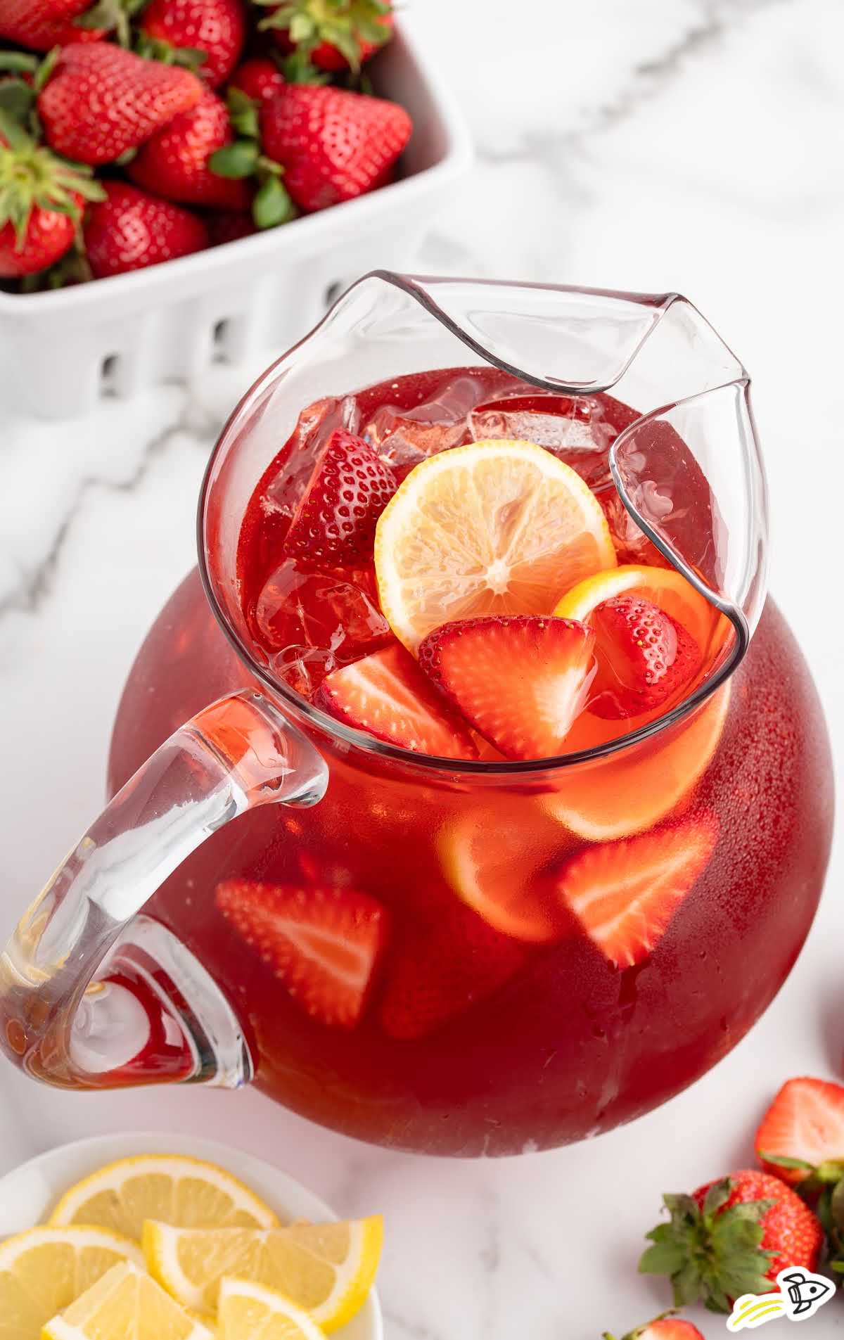 Overhead view of a glass pitcher filled with strawberry sweet tea, lemon slices, and strawberries.